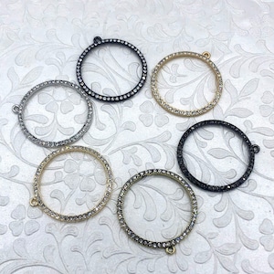 May include: Six circular jewelry findings with rhinestone accents. The findings are in various colors, including silver, gold, and black. Each finding has a small loop for attaching to other jewelry components.