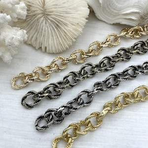 May include: Close-up of four gold and silver-toned chain necklaces. The chains have a textured, twisted link design. The background includes white coral and a white surface.