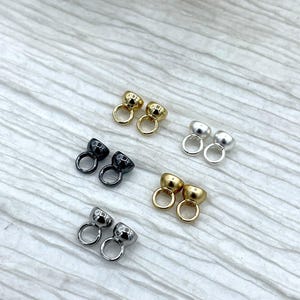May include: An assortment of small metal jewelry findings in various finishes: gold, silver, and black. Each finding features a rounded cup shape with a small loop attached, suitable for jewelry making and crafting projects.