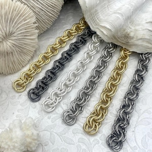 May include: Six metal chains arranged in parallel, featuring a textured, interlocking circular link design. The chains are finished in various metallic tones, including bright gold, matte black, silver, gunmetal, antique gold, and dark silver.