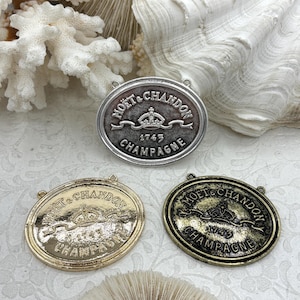 May include: Three oval-shaped metal champagne bottle labels. The labels are in silver, gold, and bronze tones. Each label has the words "MOËT & CHANDON" and "1743 CHAMPAGNE" with a crown emblem.