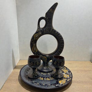 Può includere: Una tazza di ceramica bianca con manico nero e la scritta "But First, Coffee" in nero, con un carattere a mano. La tazza è su una superficie bianca.
