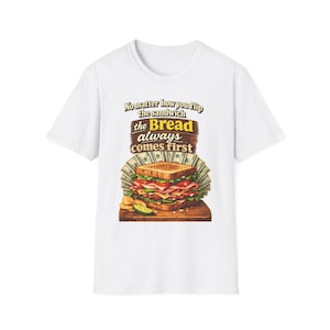 May include: White t-shirt featuring a colorful illustration of a sandwich with money and the text "No matter how you flip the sandwich the Bread always comes first."
