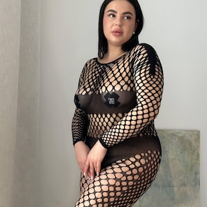 May include: Black fishnet bodysuit with long sleeves and a large open mesh design. The bodysuit covers the entire body, with a round neckline and a form-fitting silhouette. The garment has a see-through appearance.