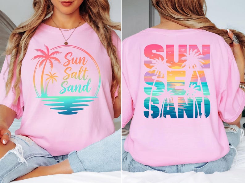K&ouml;nnte beinhalten: Hellrosa T-Shirt mit einem farbenfrohen Grafikdesign mit Palmen, Sonnenuntergang und den Worten "Sun Salt Sand" auf der Vorderseite. Auf der R&uuml;ckseite des Shirts steht "Sun Sea Sand" in einem &auml;hnlichen Design.