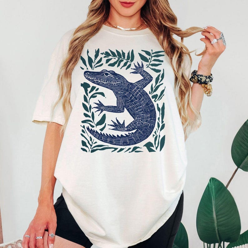 Comfort Colors ivory shirt featuring a vintage linocut style alligator surrounded by botanical leaves in a wildlife illustration printed on a garment dyed tee for reptile lovers and nature enthusiasts.