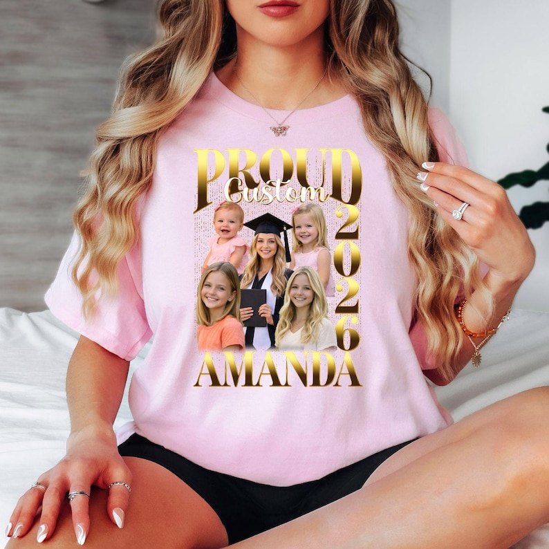 May include: A pale pink t-shirt with a gold design. The design includes the words "PROUD Custom 2020 AMANDA" and several photos. The design includes a graduation cap and multiple images of people.