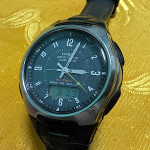 Könnte beinhalten: Eine schwarze und silberne Casio Wave Ceptor Uhr mit digitaler Anzeige, die 3:03 anzeigt. Die Uhr hat ein schwarzes Armband und ein dunkelgrünes Zifferblatt mit weißen Ziffern und Zeigern. Auf dem Zifferblatt steht "CASIO WAVE CEPTOR TOUGH SOLAR".
