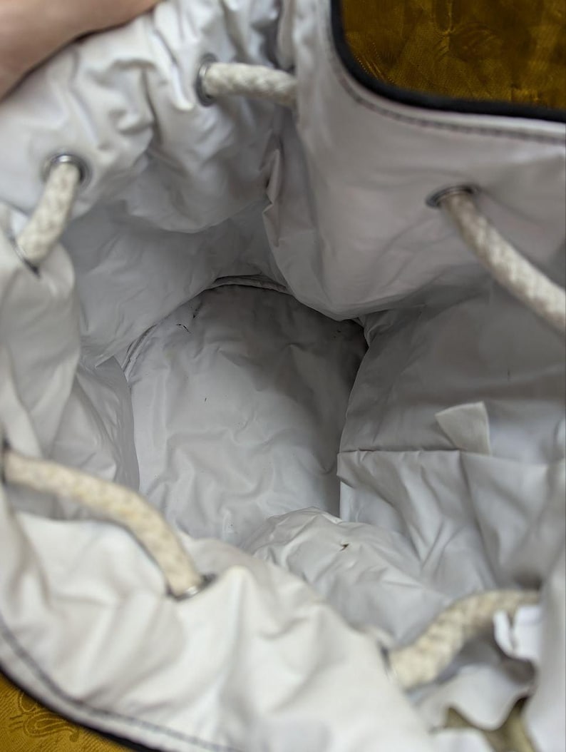 May include: A white drawstring bag with a quilted interior. The bag has a black trim and white rope drawstrings. The interior is visible, showing the quilted fabric and the drawstring closure.