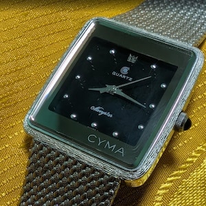 May include: A silver CYMA Quartz watch with a black square face and a silver mesh band. The watch face has silver hour markers and hands. The watch is on a yellow surface.