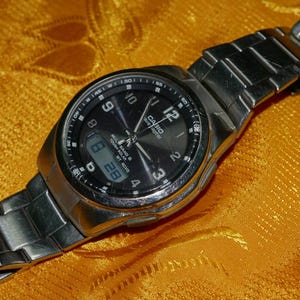May include: A silver-toned Casio Wave Ceptor wristwatch with a black analog-digital dial. The watch features a stainless steel link bracelet, luminous hands, Arabic numerals, and a digital display window showing the date 8 28.