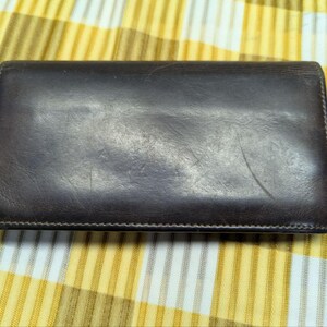 May include: A dark brown leather wallet, rectangular in shape, showing signs of wear. The wallet is closed and has a stitched border. The background is a yellow and white striped fabric.