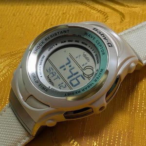 May include: A white Baby-G Wave Ceptor digital watch with a light green bezel and a matching white strap. The watch face displays the time, date, and other functions. The watch is shock resistant and water resistant.