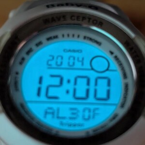 May include: A white Casio Baby-G Wave Ceptor digital watch with a blue illuminated display. The display shows the time as 12:00, date as 20/04, and other indicators. The watch has a round face and a white band.