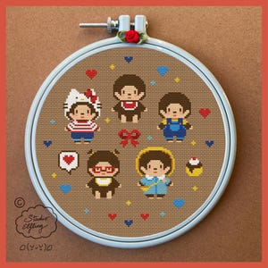 Peut inclure: Un cercle à broder au point de croix avec cinq personnages de dessins animés dans différentes tenues, dont un personnage inspiré de Hello Kitty. Le motif comprend des cœurs, des nœuds et un cupcake, le tout brodé sur un tissu marron. Le cercle est dans un cadre bleu clair.