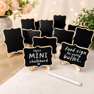 Op de afbeelding: Een set van twaalf zwarte mini-krijtbordjes met geschulpte randen en lichte houten standaards. Twee bordjes bevatten witte tekst: 12pcs MINI chalkboard en food sign for party buffet. Een witte krijtstift ligt op de voorgrond.
