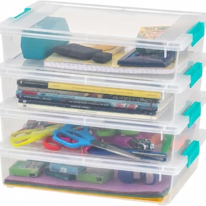 May include: A stack of four clear plastic storage bins with bright teal locking latches on the sides. The bins contain various items including notebooks, magazines, scissors, craft supplies, and colorful paper sheets visible through the transparent walls.