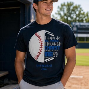 Könnte beinhalten: Ein dunkelblaues Kurzarm-T-Shirt mit einer Grafik eines Baseballs mit roten Nähten. Der Text lautet: I can do all things through Christ who strengthens me, Philippians 4:13, Lake Baseball 2026, zusammen mit einem Baseballhandschuh und Schlägern.
