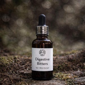 May include: A brown glass bottle with a black dropper and a white label that reads "Digestive Bitters." The label also includes the text "1oz / 30ml Extract." The bottle is set against a blurred natural background.