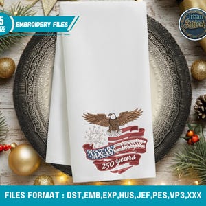 K&ouml;nnte beinhalten: Wei&szlig;es, besticktes Handtuch mit einem Adler, der amerikanischen Flagge und dem Text "We the People 250 years". Das Handtuch liegt auf einem dekorativen Teller mit Weihnachtsdekoration. Der Text "Embroidery Files" ist ebenfalls zu sehen.