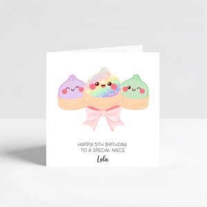 May include: A white greeting card featuring three cartoon dumplings in bamboo steamers with smiling faces. The centre dumpling is rainbow-coloured with sparkles, flanked by purple and green ones. A pink bow sits below, with text reading HAPPY 5TH BIRTHDAY TO A SPECIAL NIECE Lola.