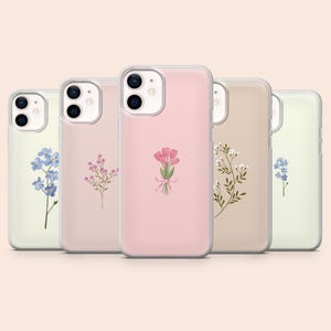 Op de afbeelding: Vijf doorzichtige smartphonehoesjes op een rij, elk voorzien van een andere delicate bloemenillustratie. De ontwerpen omvatten blauwe vergeet-mij-nietjes, kleine roze wilde bloemen, een centraal roze tulpenboeket, groene takjes en blauwe bloemen.