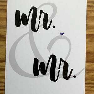 Può includere: Una carta bianca con la scritta "mr. & mr." in corsivo nero. Un cuore viola è posizionato tra le parole. La & è di colore grigio chiaro.