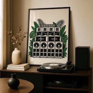 Op de afbeelding: Een ingelijste kunstprint met een zwart-witte illustratie van een gestapeld geluidssysteem, omringd door levendige groene tropische palm- en monsterabladeren, op een crèmekleurige achtergrond met een strakke zwarte lijst.
