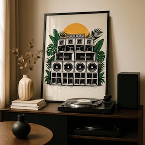 May include: A framed wall art print featuring a black and white illustration of a large sound system stack surrounded by green tropical leaves and a yellow sun, displayed on a wooden surface next to a turntable and a vase.