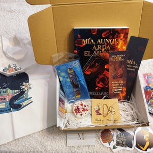 Puede incluir: Una caja de regalo llena de un libro, marcadores, pegatinas, una bolsa de mano y otros artículos pequeños. El libro tiene el título "MIA, AUNQUE ARDA EL MUNDO". La bolsa de mano tiene un gráfico de un gato negro con las palabras "LAW BOY" y "FOREVER".
