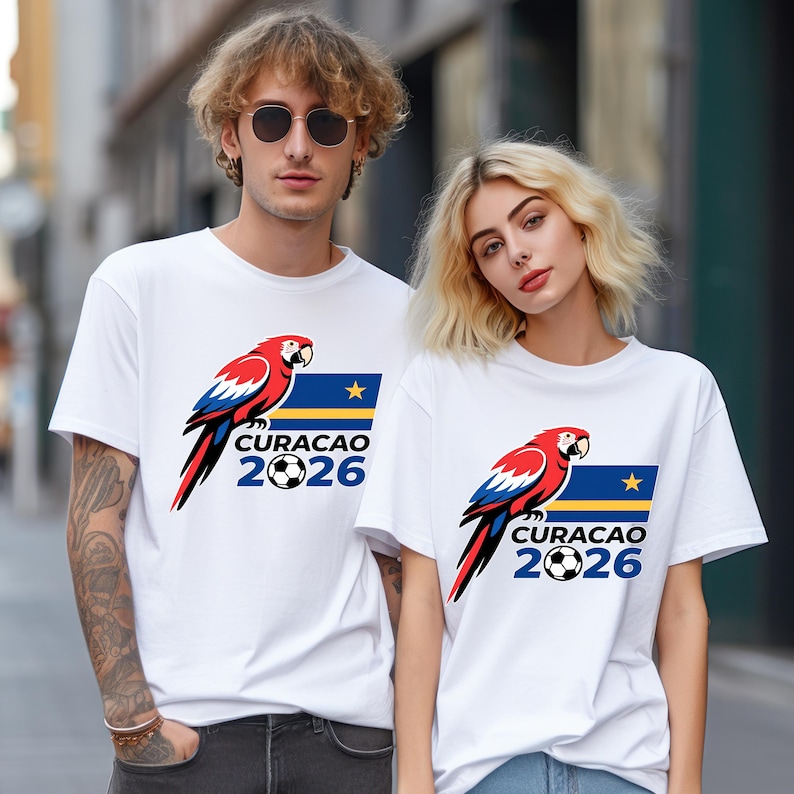 May include: White t-shirts featuring a parrot design with red, blue, and black accents. The shirts have the text "CURACAO 2026" with a soccer ball graphic, and a blue flag with a star.