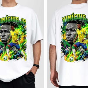 Puede incluir: Camiseta blanca con un gr&aacute;fico vibrante del futbolista Vin&iacute;cius J&uacute;nior. El dise&ntilde;o incluye un retrato y una pose de acci&oacute;n, con el nombre "Vin&iacute;cius Jr" en verde. La camiseta tiene cuello redondo y mangas cortas.