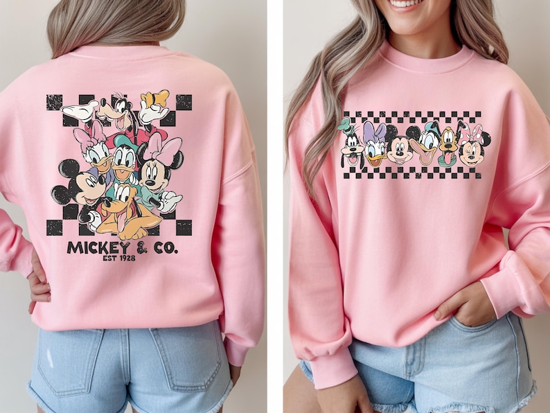 Pode incluir: Camisola rosa com um desenho do Mickey Mouse e seus amigos, incluindo Minnie, Pato Donald e Pateta, sobre um fundo xadrez preto e branco. O texto "Mickey & Co. EST 1928" est&aacute; impresso abaixo.