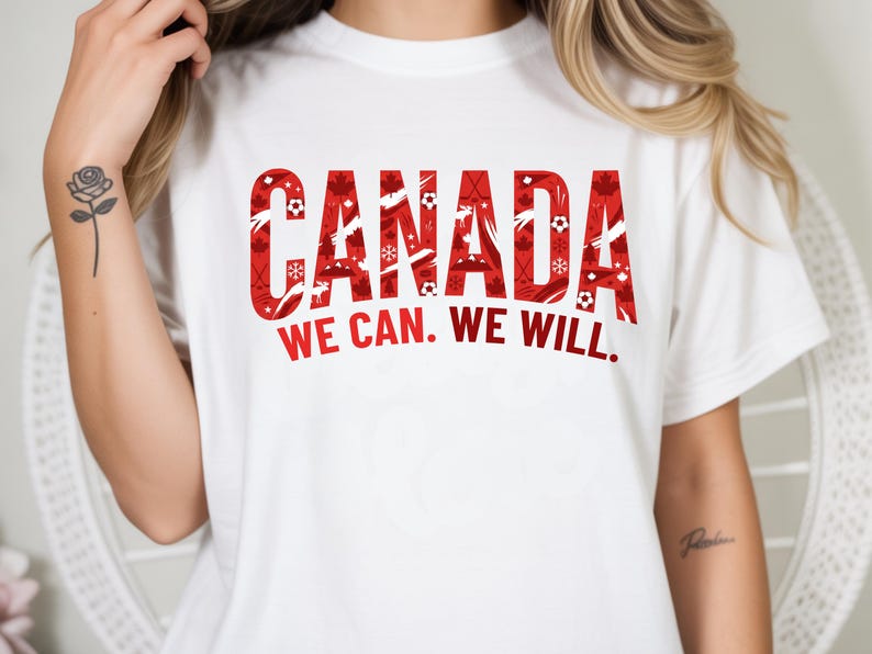May include: White t-shirt with the word "CANADA" in large red letters filled with sports and winter-themed graphics. Below the word "CANADA" is the text "WE CAN. WE WILL."