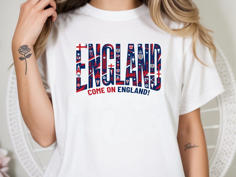 May include: White t-shirt with the word "ENGLAND" in large, stylized letters. The letters are filled with red and blue patterns and symbols. Below the word is the phrase "COME ON ENGLAND!"