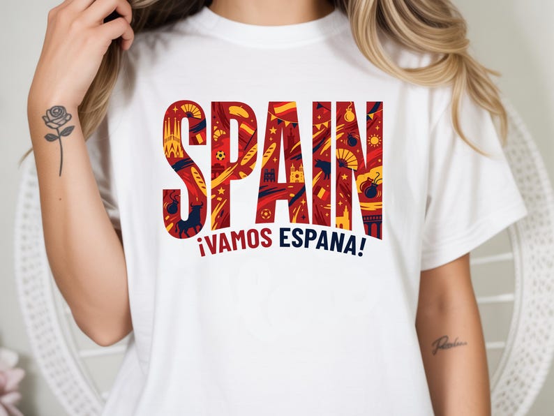 May include: White t-shirt with the word "SPAIN" in large, red letters filled with yellow and blue illustrations. Below, the phrase "&iexcl;VAMOS ESPA&Ntilde;A!" is in red and blue. The shirt is a casual wear item.