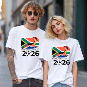 Pu&ograve; includere: T-shirt bianche con una grafica colorata raffigurante la bandiera sudafricana, un'antilope in corsa e la scritta "SOUTH AFRICA 2026" con palloni da calcio. Le magliette sono a maniche corte.