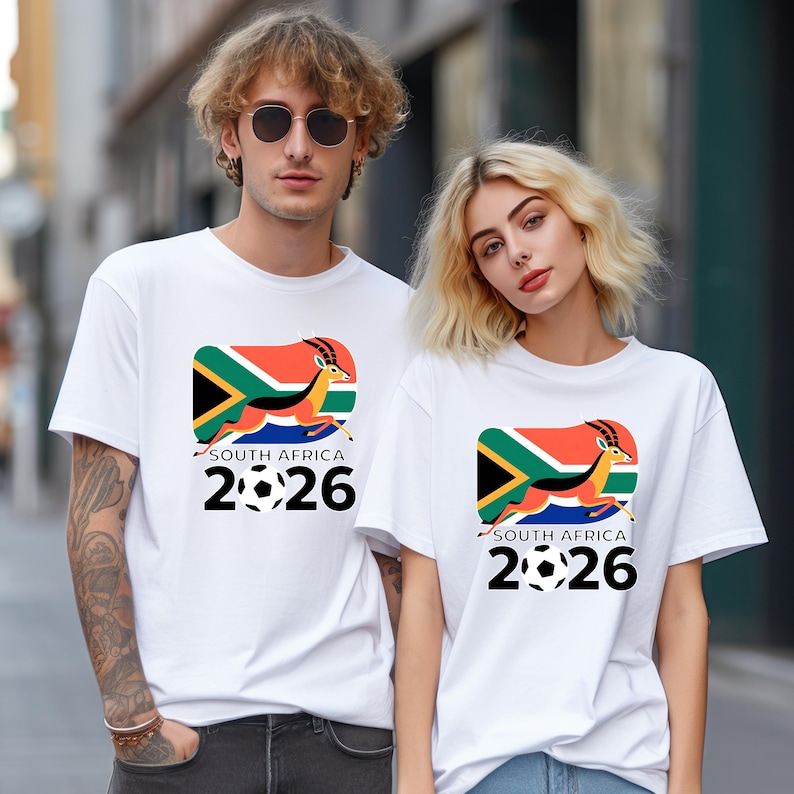 Pu&ograve; includere: T-shirt bianche con una grafica colorata raffigurante la bandiera sudafricana, un'antilope in corsa e la scritta "SOUTH AFRICA 2026" con palloni da calcio. Le magliette sono a maniche corte.