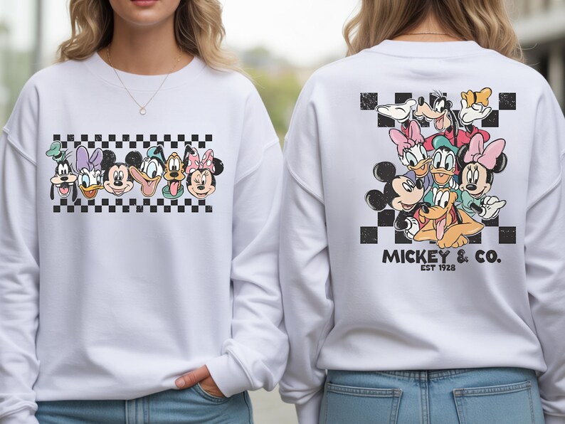 Pode incluir: Camisola branca com um gr&aacute;fico do Mickey Mouse e seus amigos. O design frontal apresenta rostos de personagens em um padr&atilde;o xadrez preto e branco. O design traseiro apresenta um grupo de personagens com o texto "Mickey & Co. EST 1928".