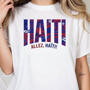 May include: White t-shirt featuring the word "HAITI" in bold, stylized letters with a red, white, and blue pattern. The text "ALLEZ, HAITI!" is printed below. The shirt has short sleeves.