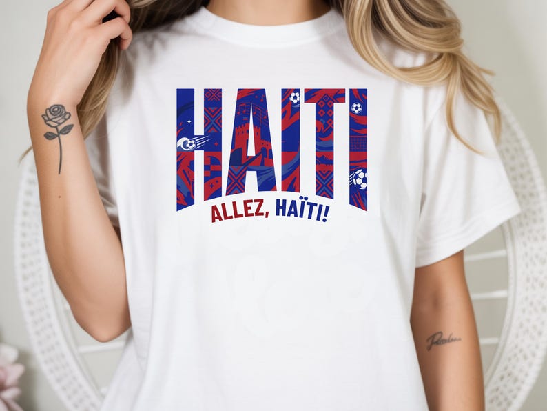 May include: White t-shirt featuring the word "HAITI" in bold, stylized letters with a red, white, and blue pattern. The text "ALLEZ, HAITI!" is printed below. The shirt has short sleeves.