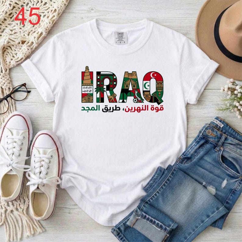 Puede incluir: Una camiseta blanca de manga corta con la palabra IRAQ en letras grandes, cada una rellena con ilustraciones coloridas de monumentos y s&iacute;mbolos culturales, con texto en &aacute;rabe impreso debajo en tinta verde y roja.