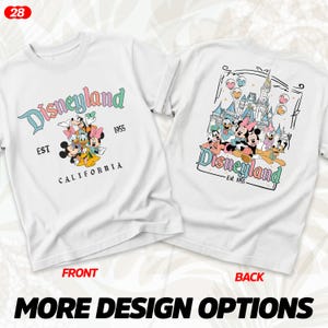 Puede incluir: Camiseta blanca con el logo de Disneyland y personajes. El frente muestra el logo de Disneyland, personajes y el texto "Est 1955 California". La parte posterior presenta un castillo y m&aacute;s personajes.