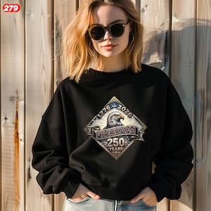 Pode incluir: Camisola preta com um design patri&oacute;tico de &aacute;guia e o texto "Freedom 250 Years", com os anos 1776-2026. O design usa azul, dourado e branco. A camisola &eacute; usada por uma pessoa.