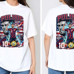 Puede incluir: Camiseta blanca con un gr&aacute;fico de un jugador de f&uacute;tbol con una camiseta a rayas rojas y azules, con el nombre "Pulisic" y el n&uacute;mero "10". El dise&ntilde;o incluye la bandera estadounidense y un bal&oacute;n de f&uacute;tbol.