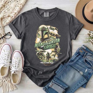 May include: Dark gray t-shirt featuring a graphic from "The Mandalorian" with the text "The Mandalorian and Grogu" and "This is the Way." The design includes images of the Mandalorian and Grogu.