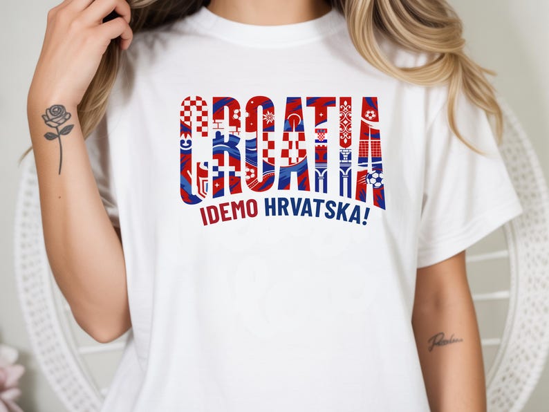 May include: White t-shirt with the word "CROATIA" in red, white, and blue, with various Croatian flag-inspired patterns filling each letter. Below the word is the phrase "IDEMO HRVATSKA!" in red. The shirt is a casual wear item.