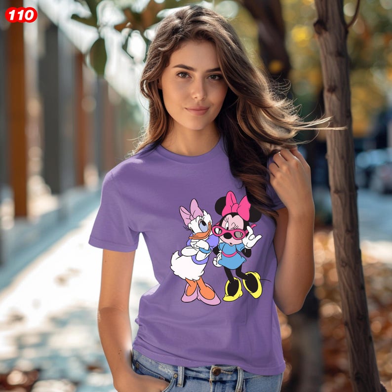 Pode incluir: Uma camiseta roxa com um gr&aacute;fico da Minnie Mouse e da Margarida. Minnie Mouse usa &oacute;culos rosa e um la&ccedil;o rosa. Margarida tem um la&ccedil;o azul. O n&uacute;mero "110" est&aacute; no canto superior esquerdo.