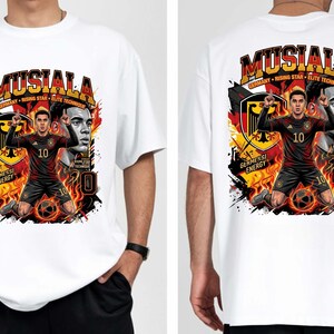 Puede incluir: Camiseta blanca con un gr&aacute;fico de un jugador de f&uacute;tbol con uniforme negro y rojo, con el nombre "Mustala" arriba. El dise&ntilde;o incluye la bandera alemana y el texto "Germany Rising Star Elite Technique".