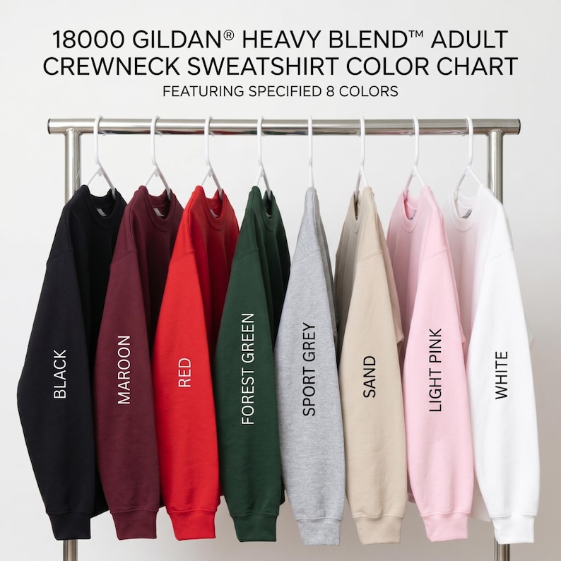 May include: A Gildan 18000 Heavy Blend crewneck sweatshirt color chart featuring eight long-sleeve shirts hanging on white plastic hangers. The colors displayed from left to right are black, maroon, red, forest green, sport grey, sand, light pink, and white.